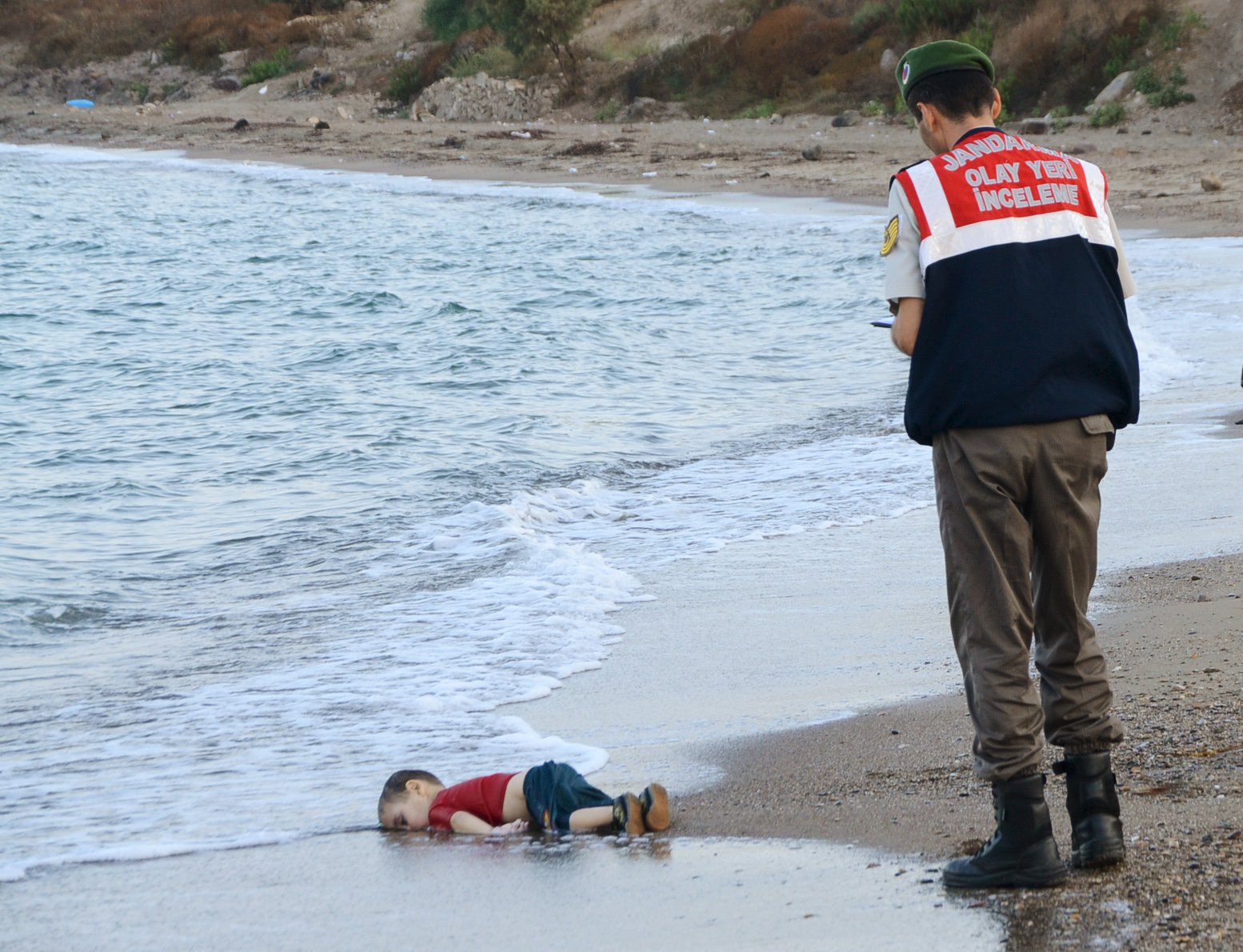 A Turkish gendarmerie stands next to a young migrant, who drowned in a failed attempt to sail to the Greek island of Kos, as he lies on the shore in the coastal town of Bodrum, Turkey